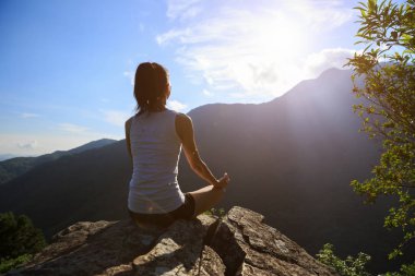 Dağ tepe uçurumun kenarında güneşin doğuşunu meditasyon yoga kadın