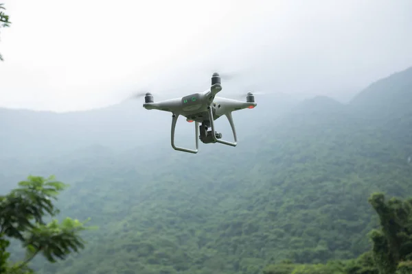 White drone with camera flying over forest