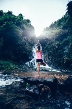 Genç kadın şelale orman içinde yakınındaki Yoga uygulamak