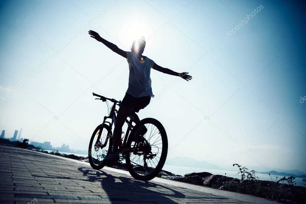 Hands free cycling woman riding Mountain Bike on sunrise seaside