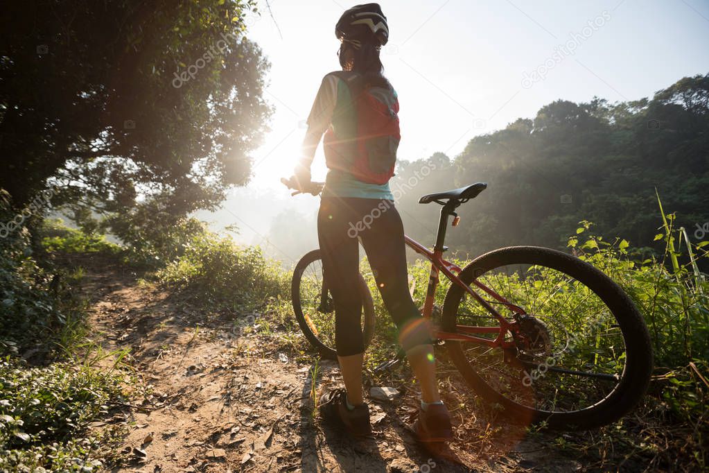 Young woman cyclist carrying mountain bike on summer forest trail