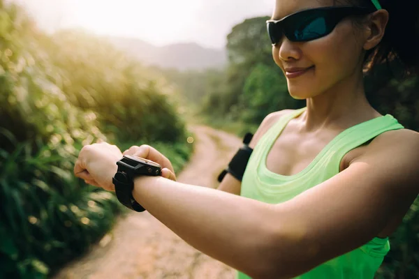 Asian woman setting the sports watch before trail running on mountain