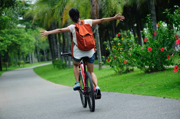骑自行车的妇女在阳光明媚的公园小径上伸出双臂 — 图库照片