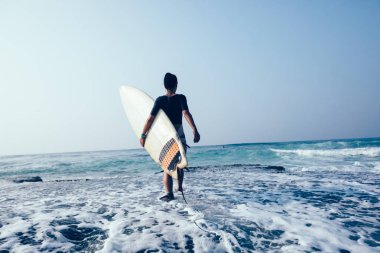 Kadın sörfçü yosunlu deniz kıyısı kayalıkları üzerinde yürüme surfboard ile