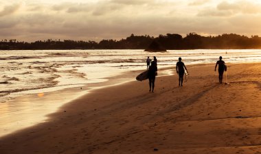 Güzel gün batımı sırasında kum plajındaki sörfçü siluetleri 