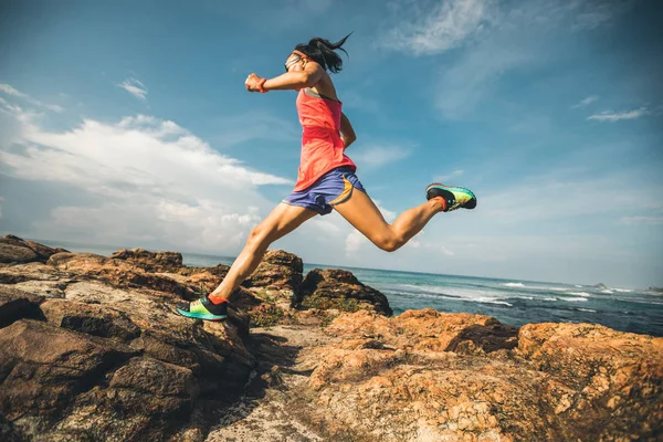 Young fitness woman trail runner running to rocky mountain top on seaside