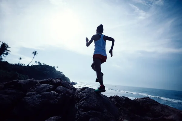 Woman trail runner running at rocky mountain top on seaside