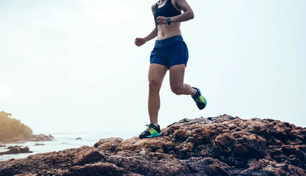 Woman trail runner running at rocky mountain top on seaside