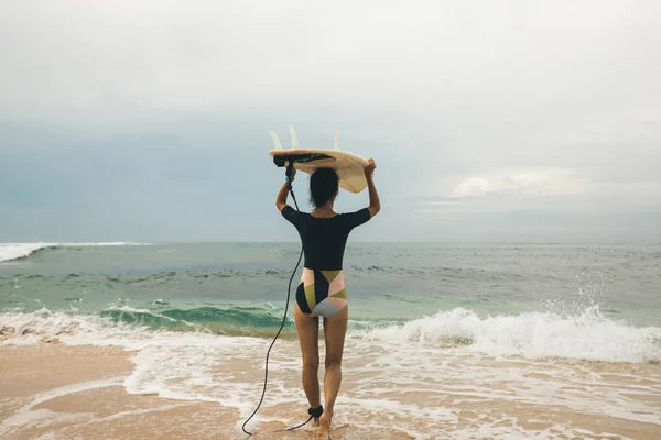 Surfer woman with surfboard walking on tropical beach