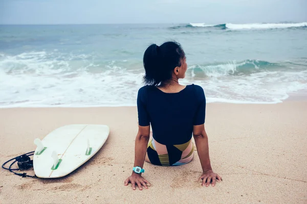 Surfer woman with surfboard relaxing on tropical beach