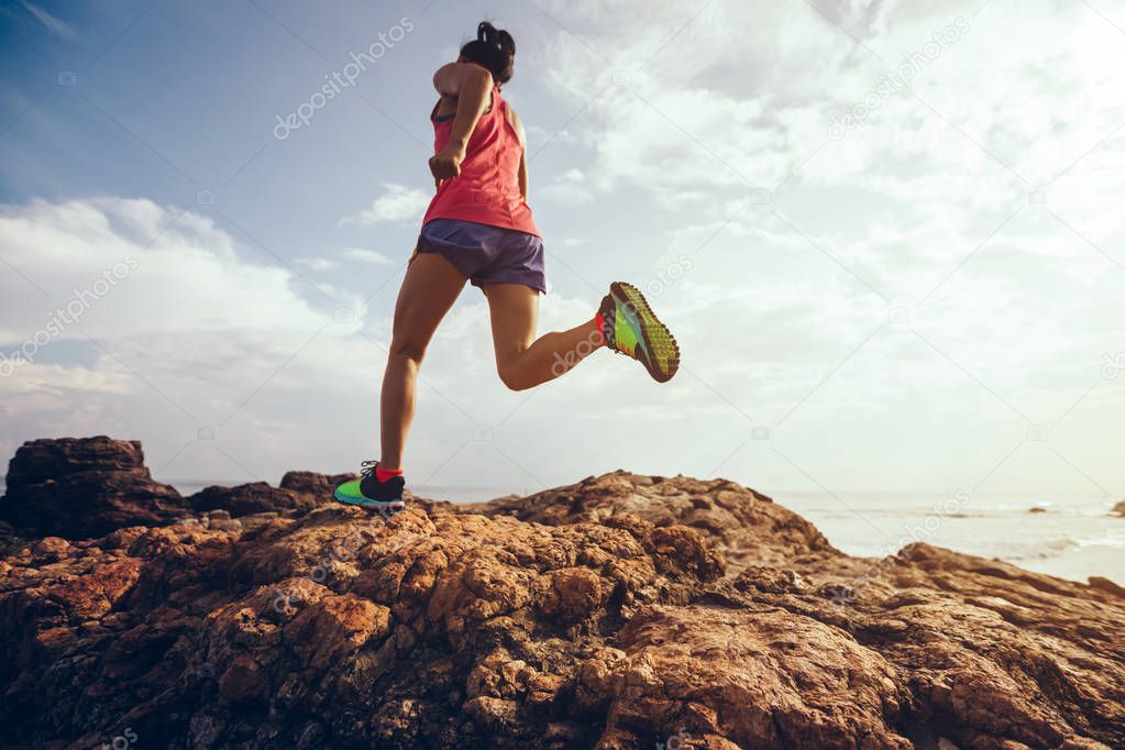 Young fitness woman trail runner running to rocky mountain top on seaside