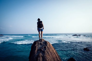 Genç kadın backpacker sahil rock uçurumun kenarında aşağı bakıyor