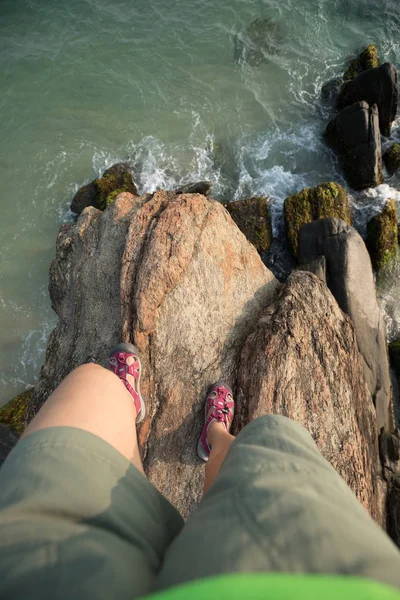 human legs stand on rock cliff edge at seaside