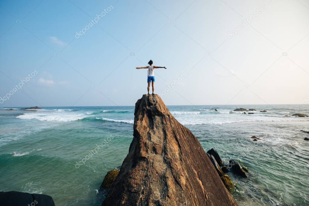 Freedom young woman with outstretched arms standing on seaside rock