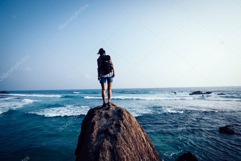 Young woman backpacker on seaside rock cliff edge looking down