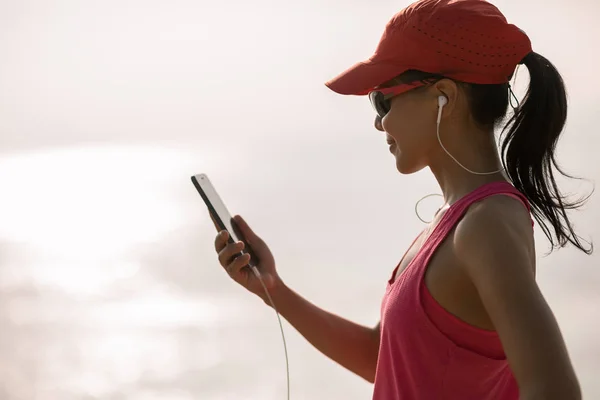 フィットネス スポーツウーマンが日当たりの良い海岸に携帯電話で音楽を聴く — ストック写真