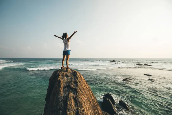 Successful young woman with outstretched arms on seaside rock cliff edge