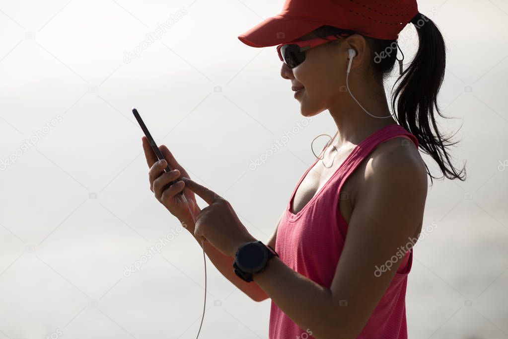 Fitness sportswoman listening music with mobile phone on sunny coast