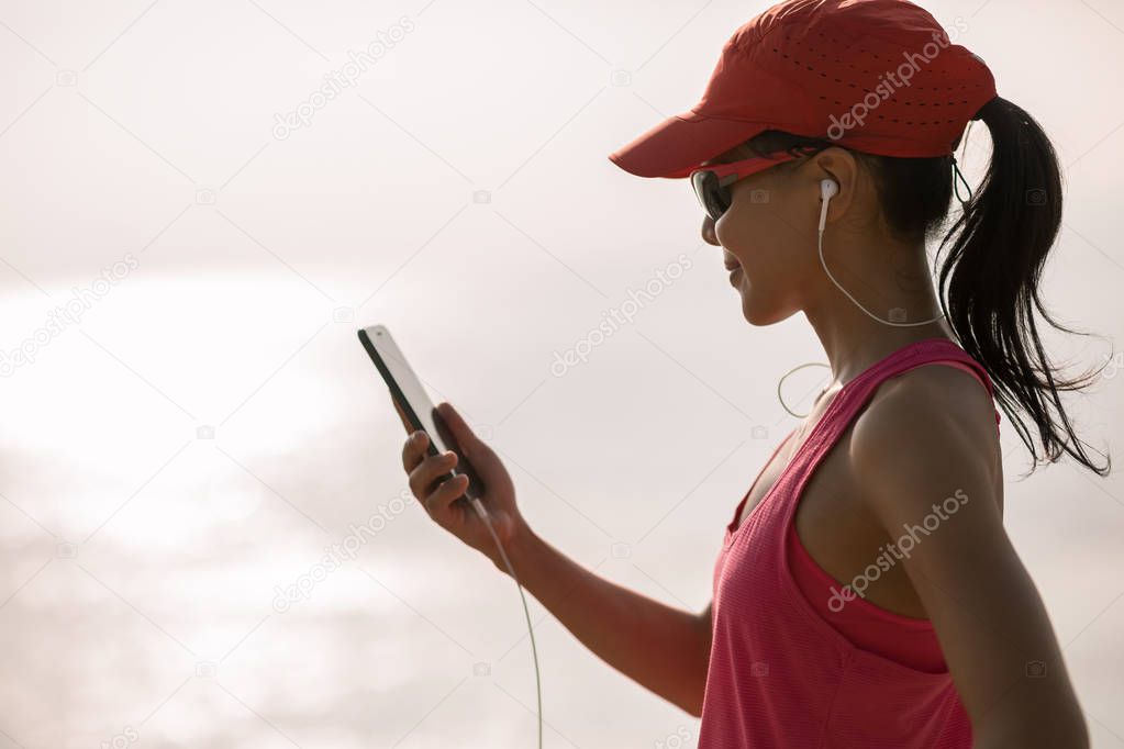 Fitness sportswoman listening music with mobile phone on sunny coast