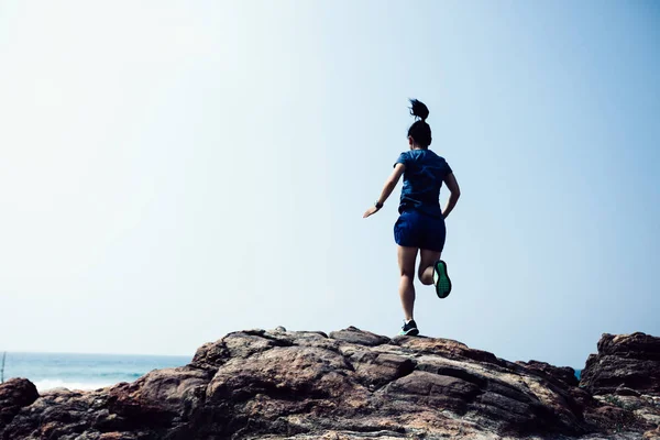 Woman trail runner running to rocky mountain top on seaside
