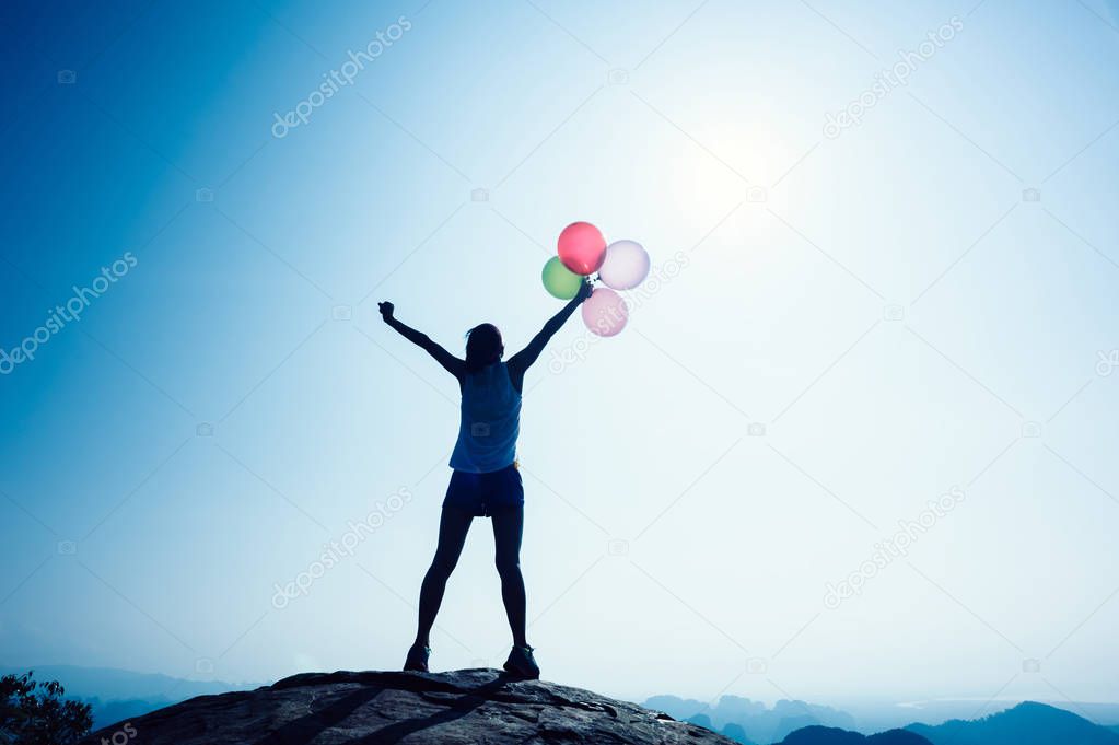 Freedom woman with balloons on sunrise mountain top edge 