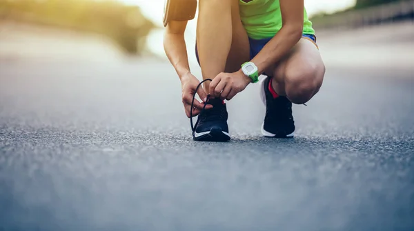 Sportswoman tying shoelace before running on city street