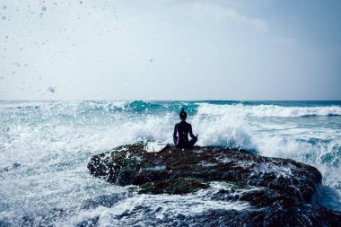 Kadın sörfçü meditasyon önümüzdeki güçlü deniz dalgaları karşı karşıya sahil mercan kayalığı kenarında