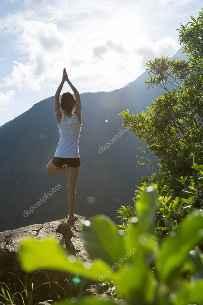 Yoga woman meditating on mountain peak cliff edge in sunrise