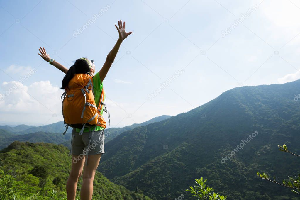 Cheering woman backpacker enjoying the view from mountain peak