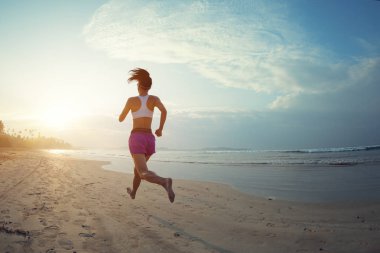 Genç fitness kadını gün doğumunda plajda koşuyor. 
