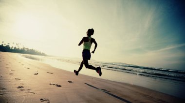Güneş doğarken plajda koşan fitness kadın koşucusu 