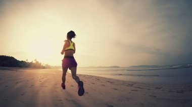 Güneş doğarken plajda koşan fitness kadın koşucusu 