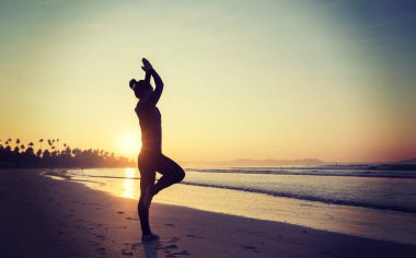 Güneş doğarken plajda yoga yapan bir kadın.
