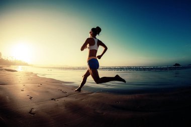 Genç fitness kadını gün doğumunda plajda koşuyor. 