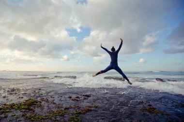 Sahilde atlayan sörf kıyafetli kadın.