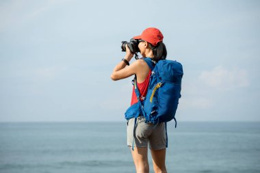 Kadın fotoğrafçı Deniz kenarında yürüyüş yapıyor ve kamerayla fotoğraf çekiyor.  