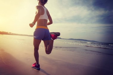 Genç fitness kadını gün doğumunda plajda koşuyor. 