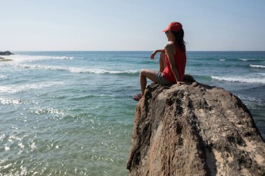 Deniz kenarında uçurumun kenarında oturan cesur kadın 