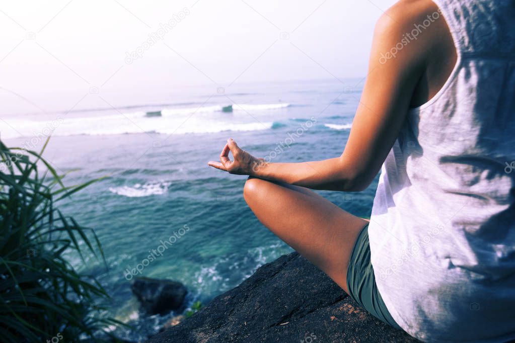 Woman practicing yoga at seaside on the rock 