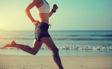 Genç fitness kadını gün doğumunda plajda koşuyor. 