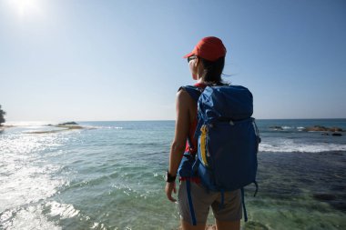 Sırt çantalı kadın denizin yanındaki alacakaranlık gökyüzüne bakıyor.