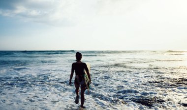 Surfboard ile sahil üzerinde yürüyen sörfçü kadın