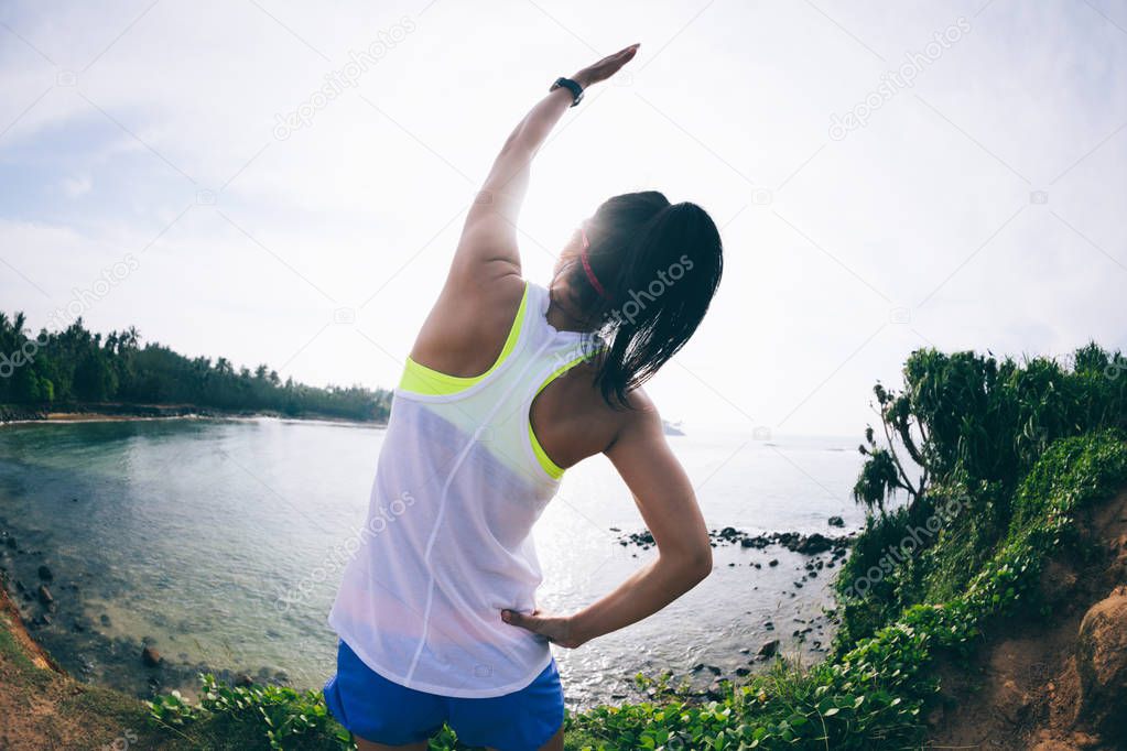 young fitness woman stretching arms on seaside cliff