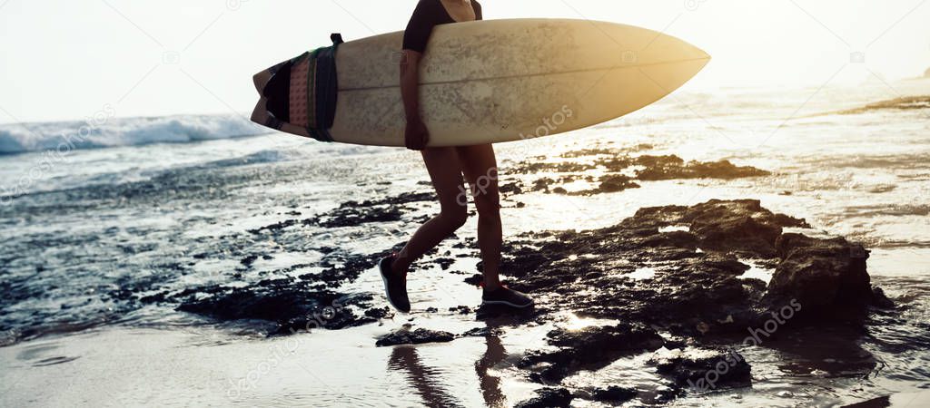 Surfer woman walking with surfboard on seaside