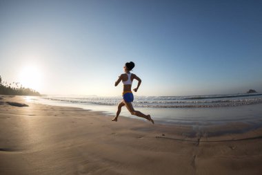 Genç fitness kadını gün doğumunda plajda koşuyor. 