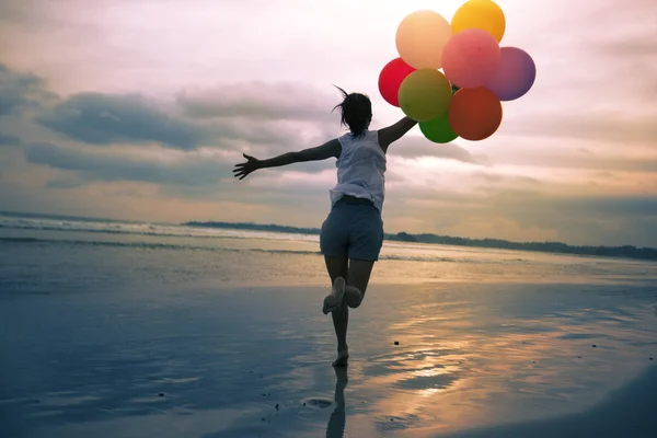 色付きの風船で海辺に走ったり飛び降りたりする若い女性 — ストック写真