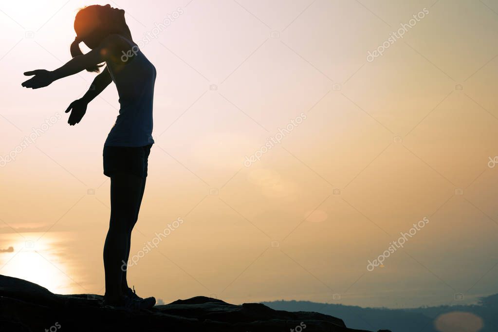 cheering woman with open arms at sunset mountain top