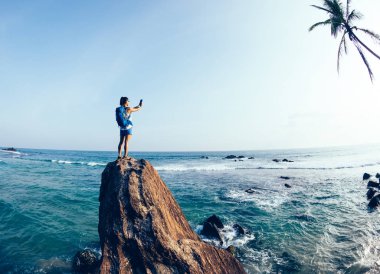 Sahil kaya uçurumun kenarına fotoğraf çekerken genç kadın turist 
