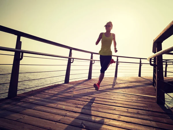 日出时跑在海滨木板路上的体态健壮的女跑步者 — 图库照片