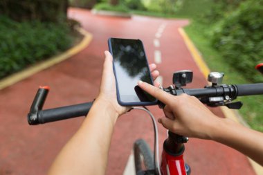 orman yolunda bisiklete binerken navigasyon için akıllı telefon uygulamasını kullanan kişi